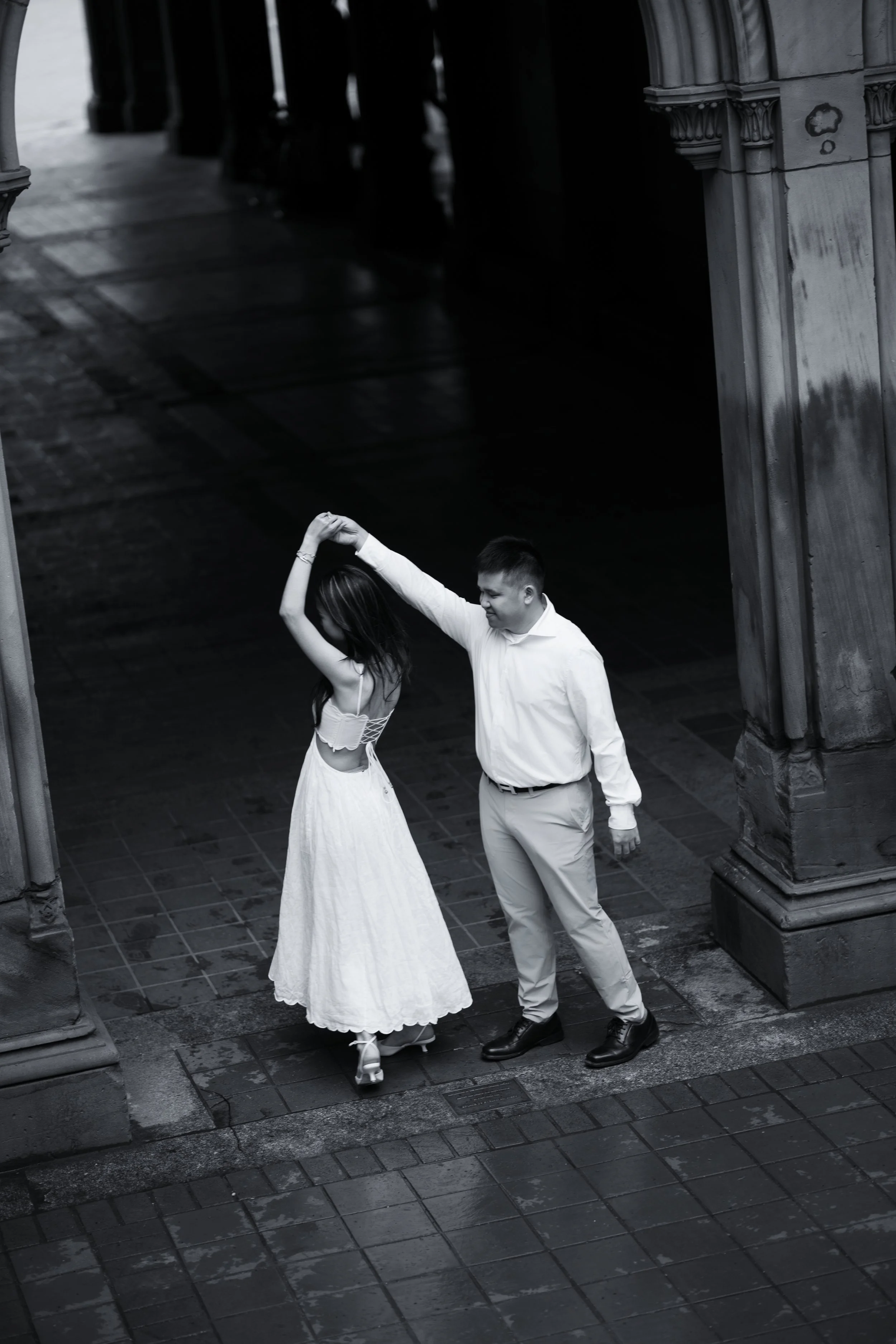 A black and white photo of a man and woman dancing together in a courtyard, with the man holding the woman's hand above her head.