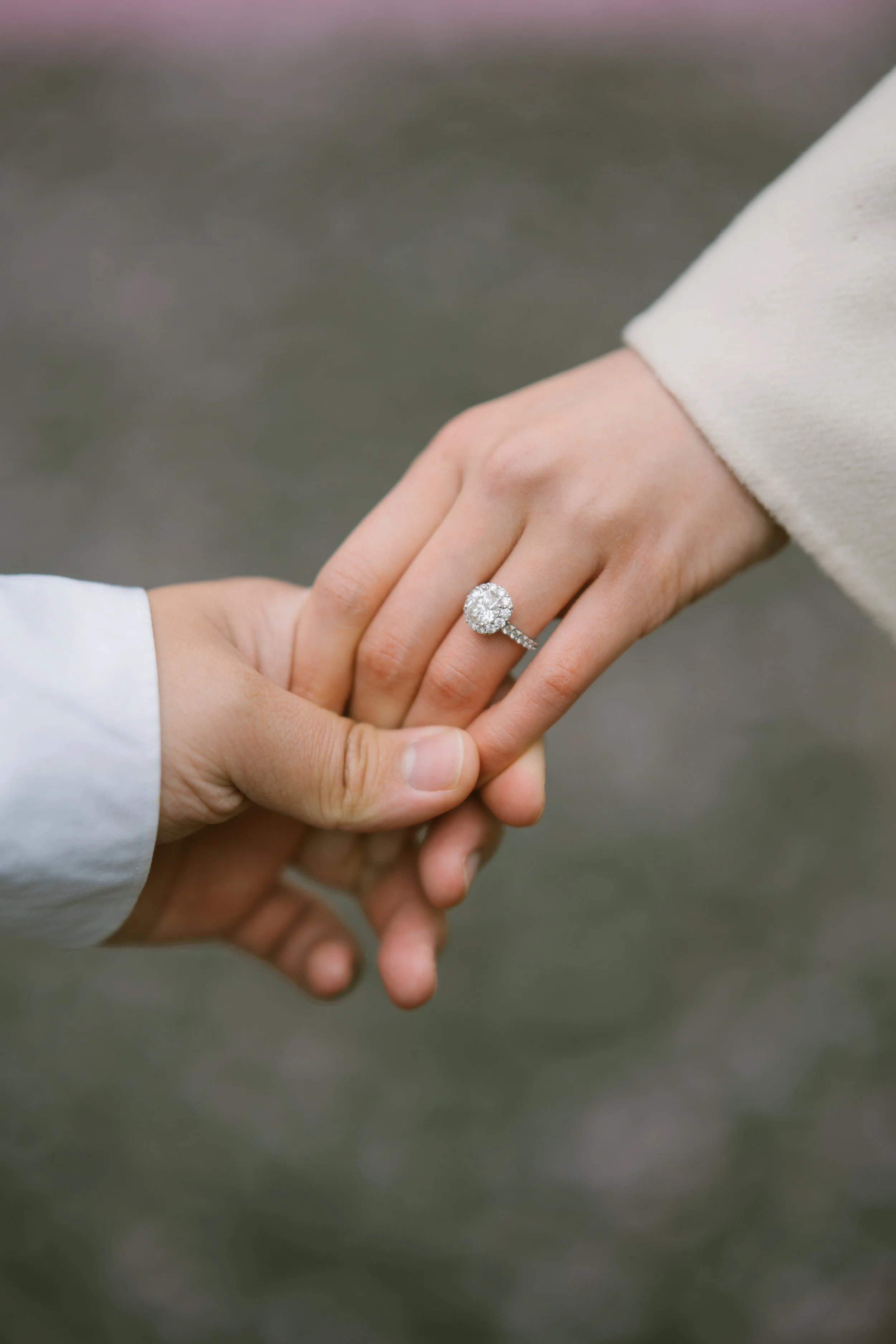Two hands holding each other, with one hand wearing a large diamond engagement ring.