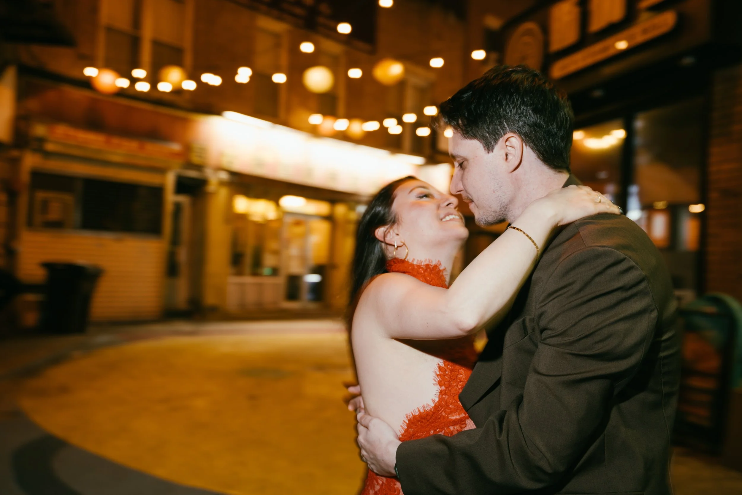 A couple dancing closely in a dimly lit venue with warm string lights overhead.