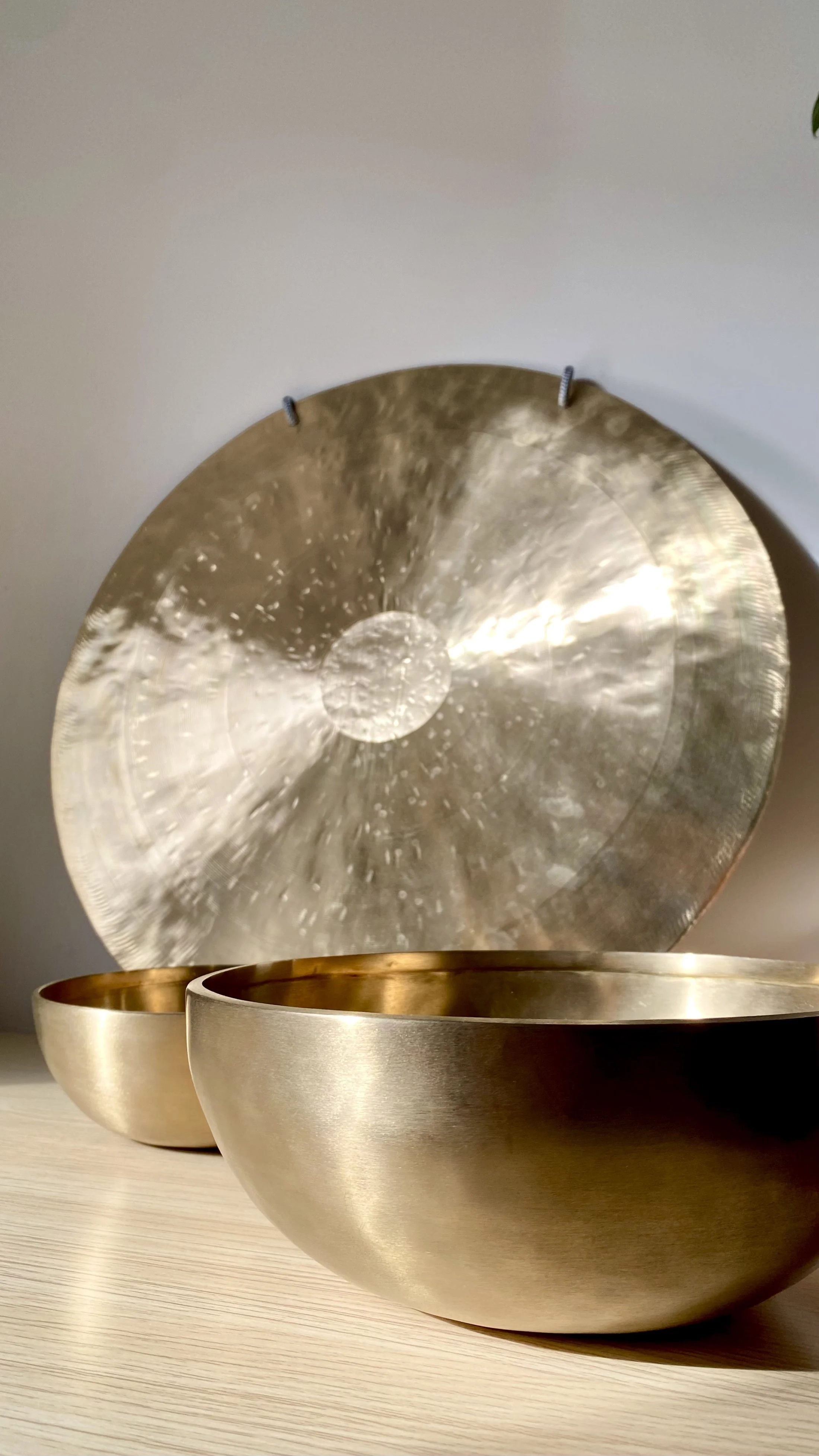 Brass-coloured therapeutic gong and sound bowls, on wooden surface against white wall
