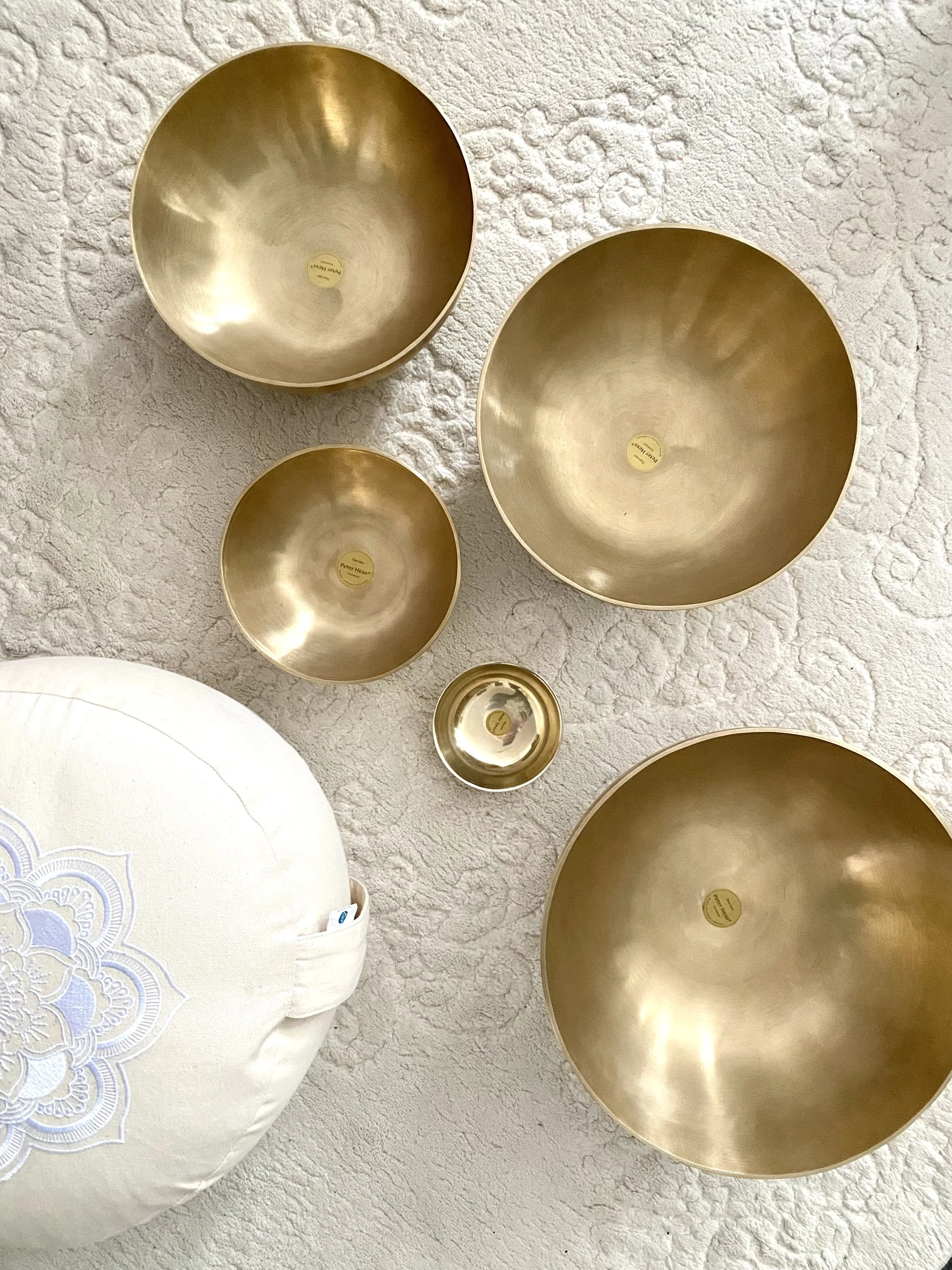 Brass-coloured therapeutic singing bowls on cream coloured rug