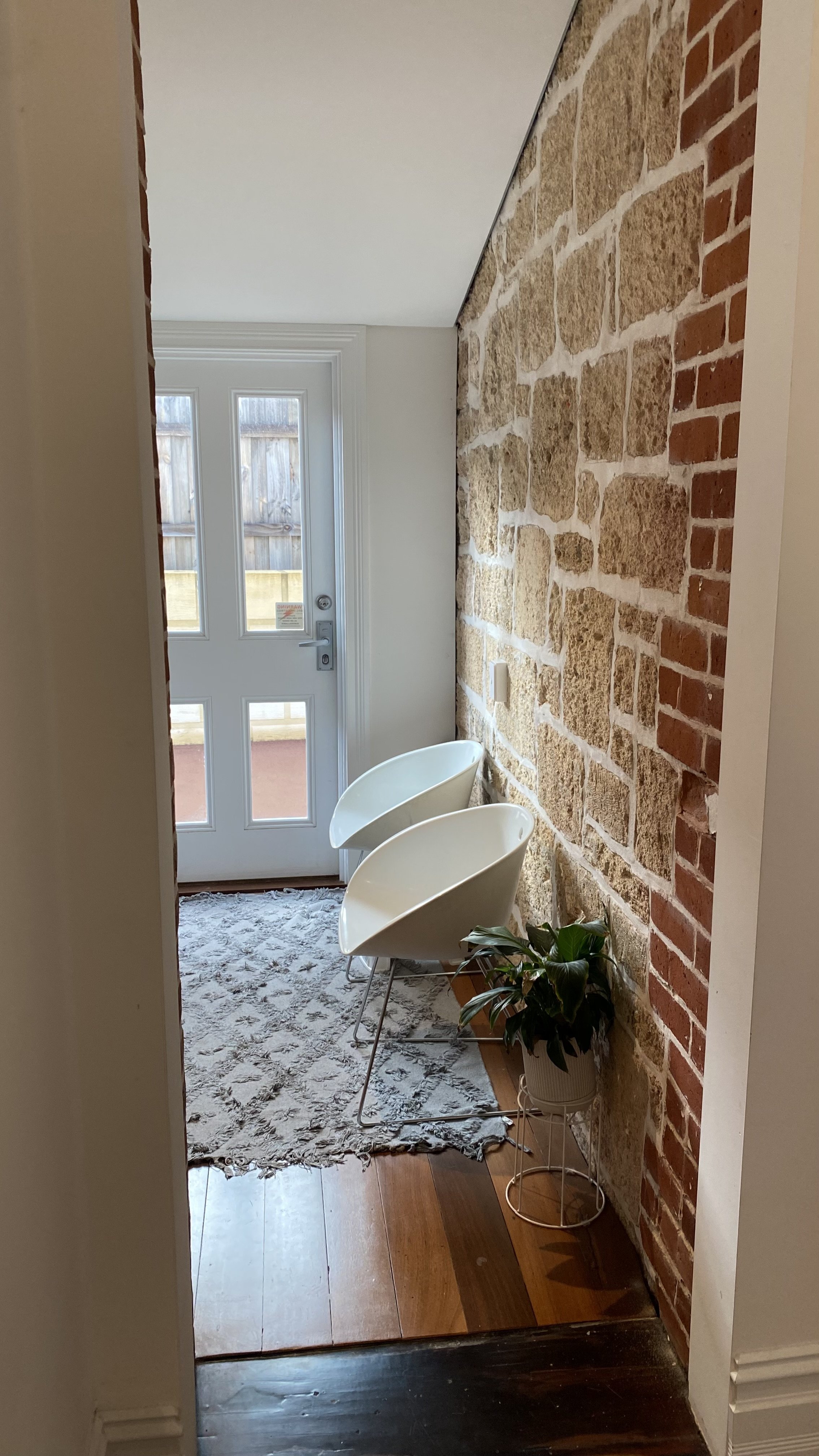 Image of entry way/waiting room with white door and two white chairs against stone wall