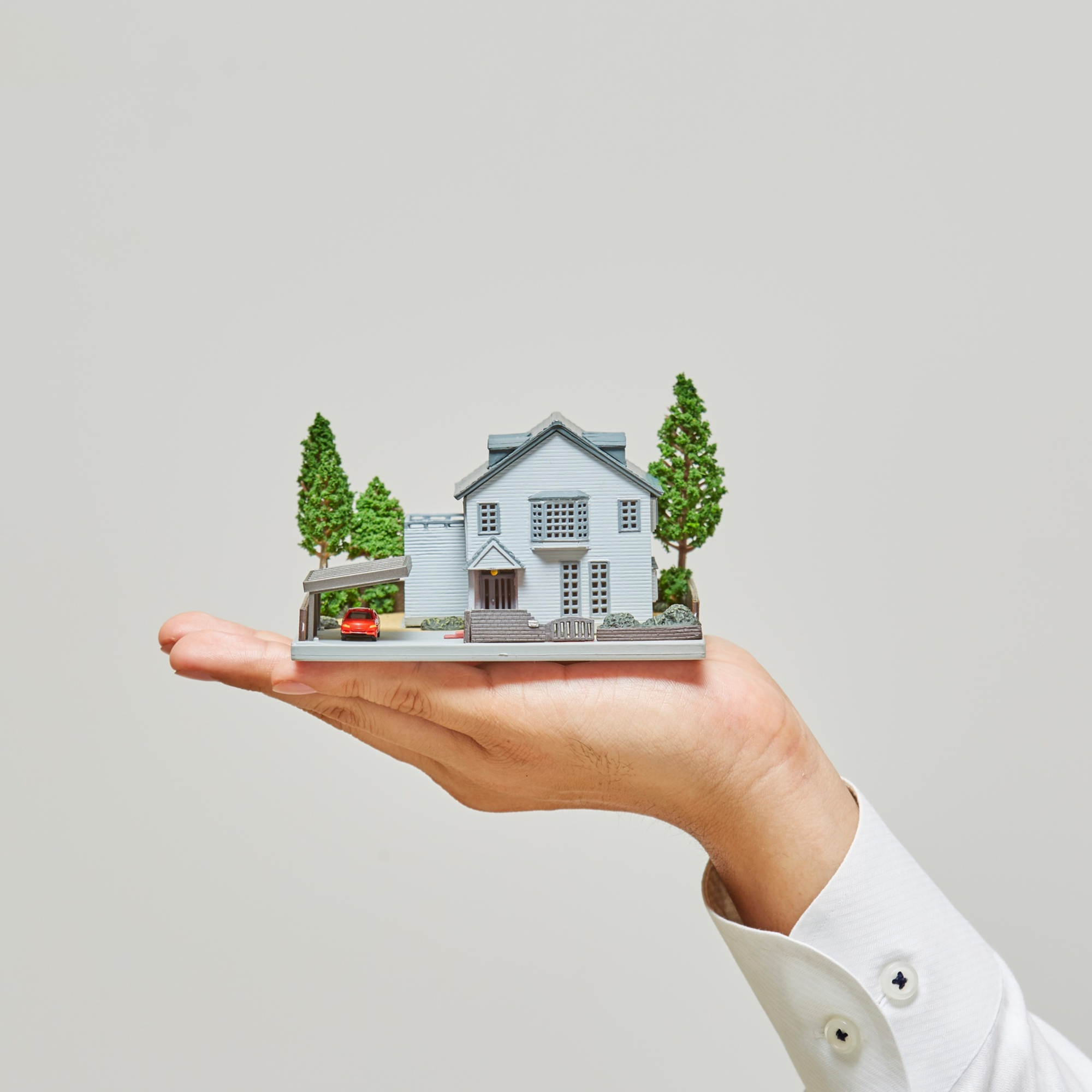 Smaller house model with trees and a miniature car in a person's hand.