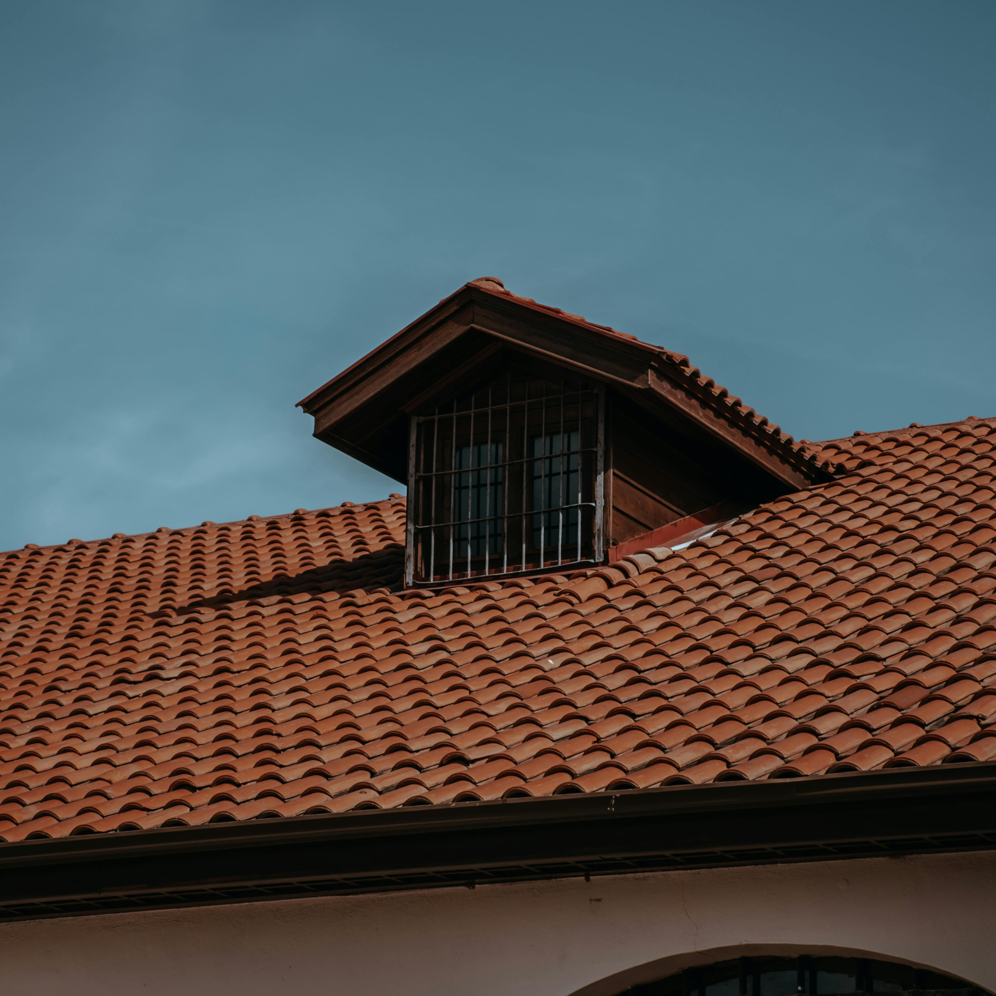 A construction worker installing shingles on a roof, wearing a safety harness and gloves.