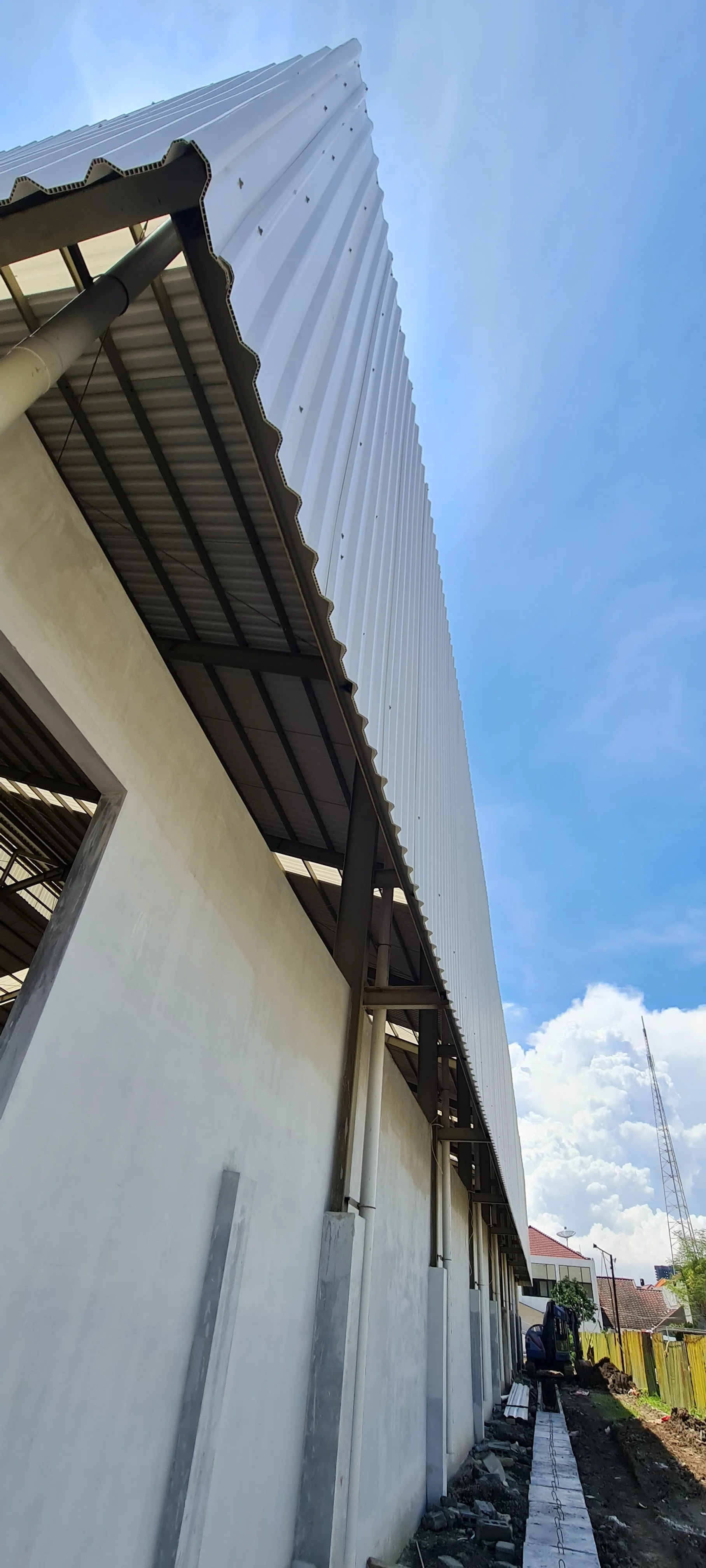Low-angle view of a large building with a metal roof, under construction, with a partly cloudy sky in the background.