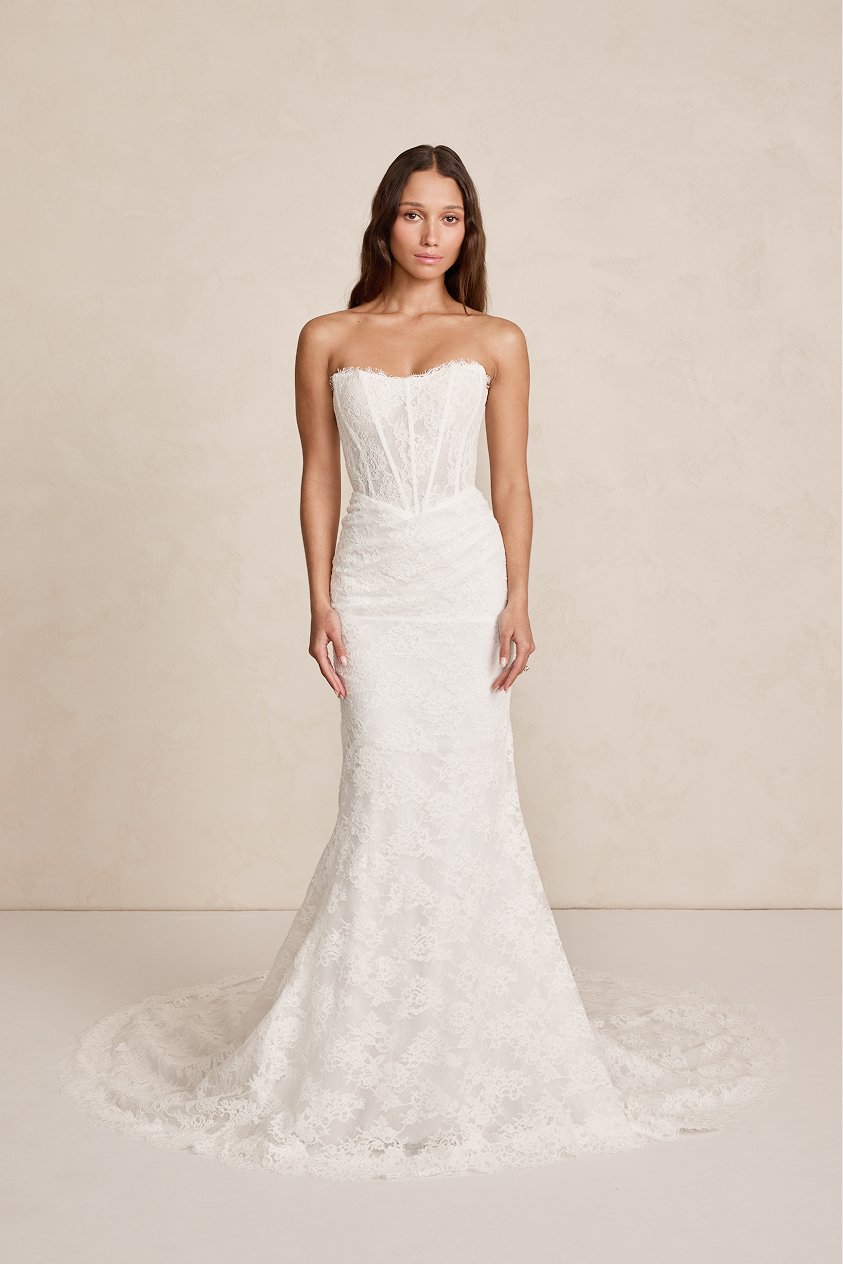 A woman wearing a white strapless lace wedding gown with a fitted silhouette and a train.