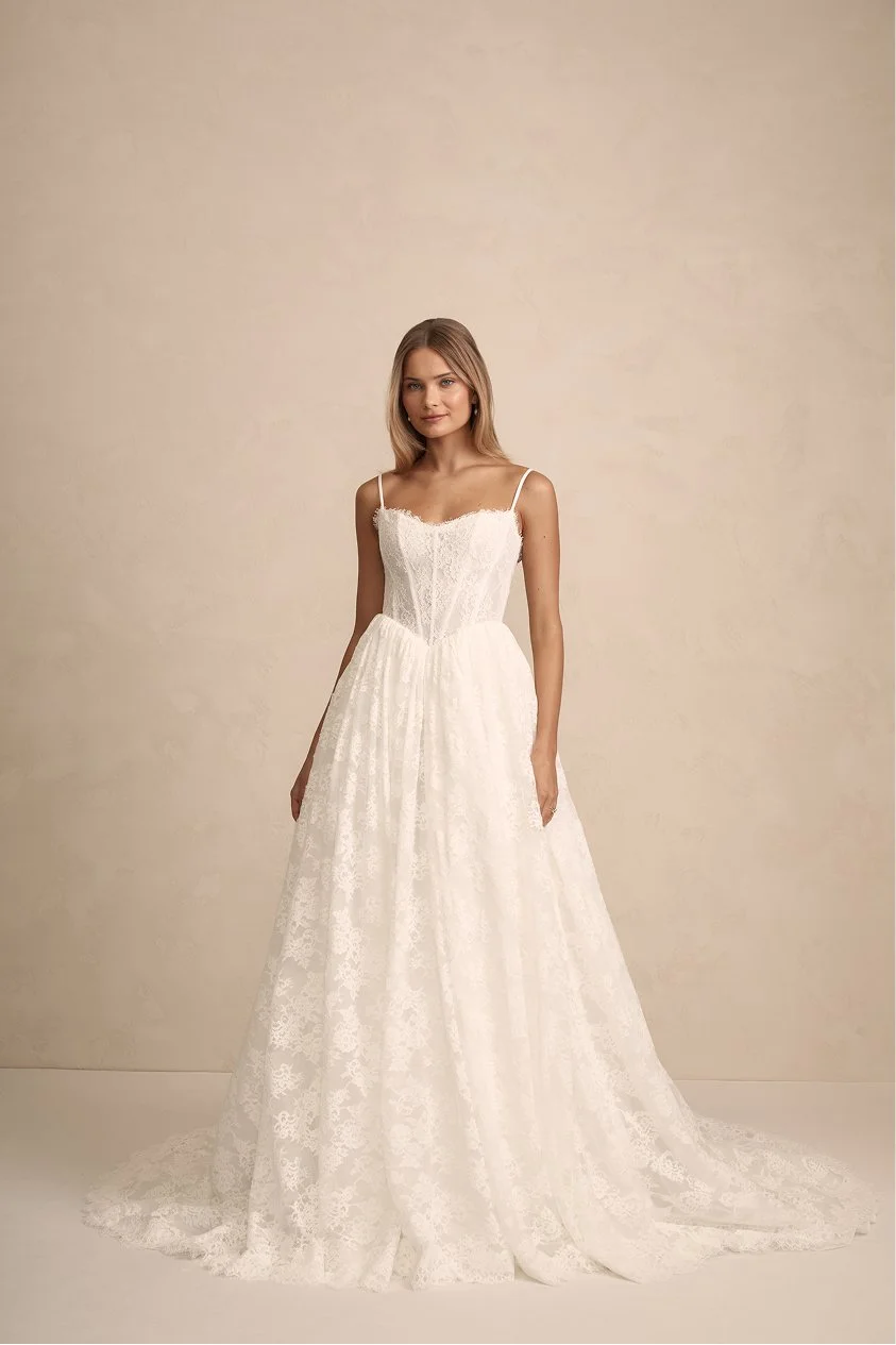 A woman in a white wedding dress standing against a beige background.