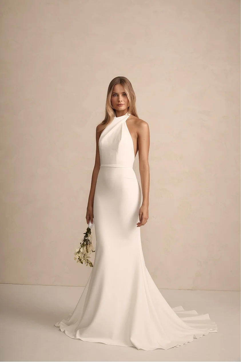 A woman in a sleek, white wedding gown holding a small bouquet of flowers.