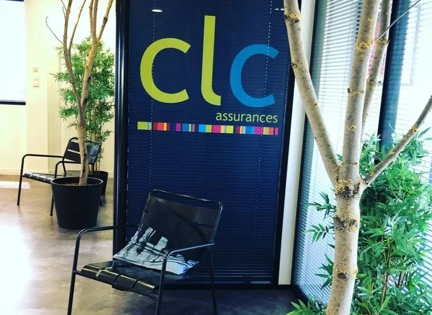 Une salle d'attente avec des chaises, des plantes vertes et un panneau avec le logo de CLC Assurances.