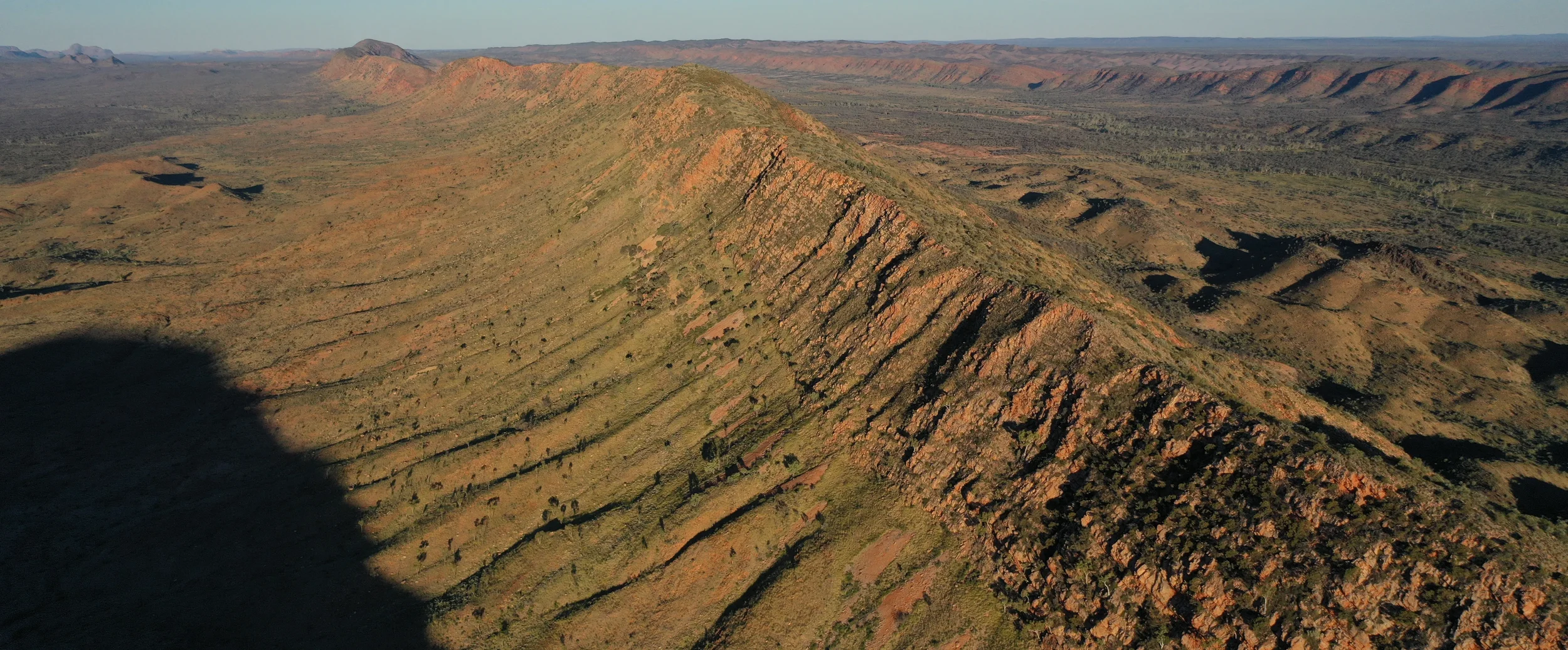 Aerial view of a mountain ridge in a desert landscape with rolling hills in the distance.