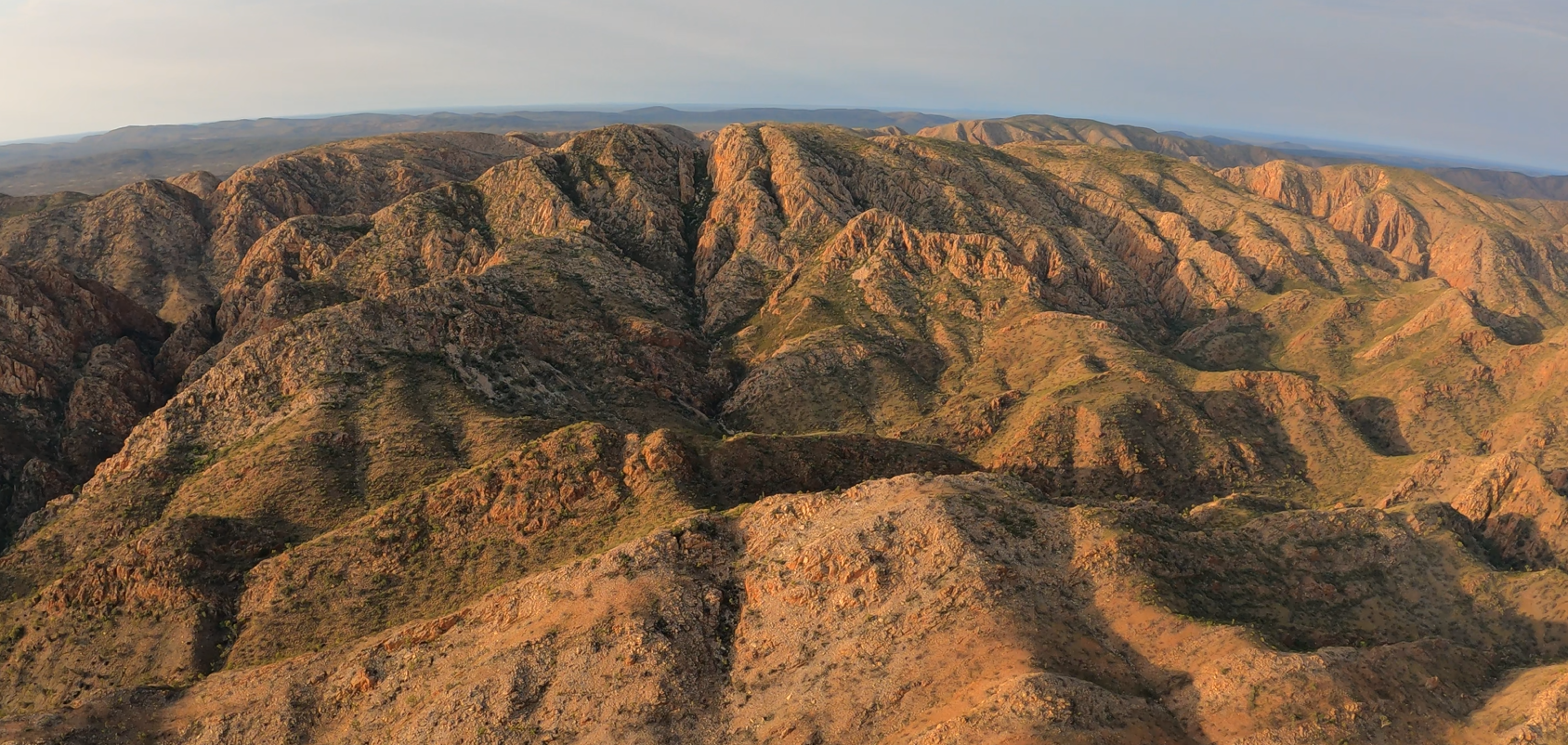 A panoramic view of rugged, rocky mountains with patches of green vegetation, under a cloudy sky.