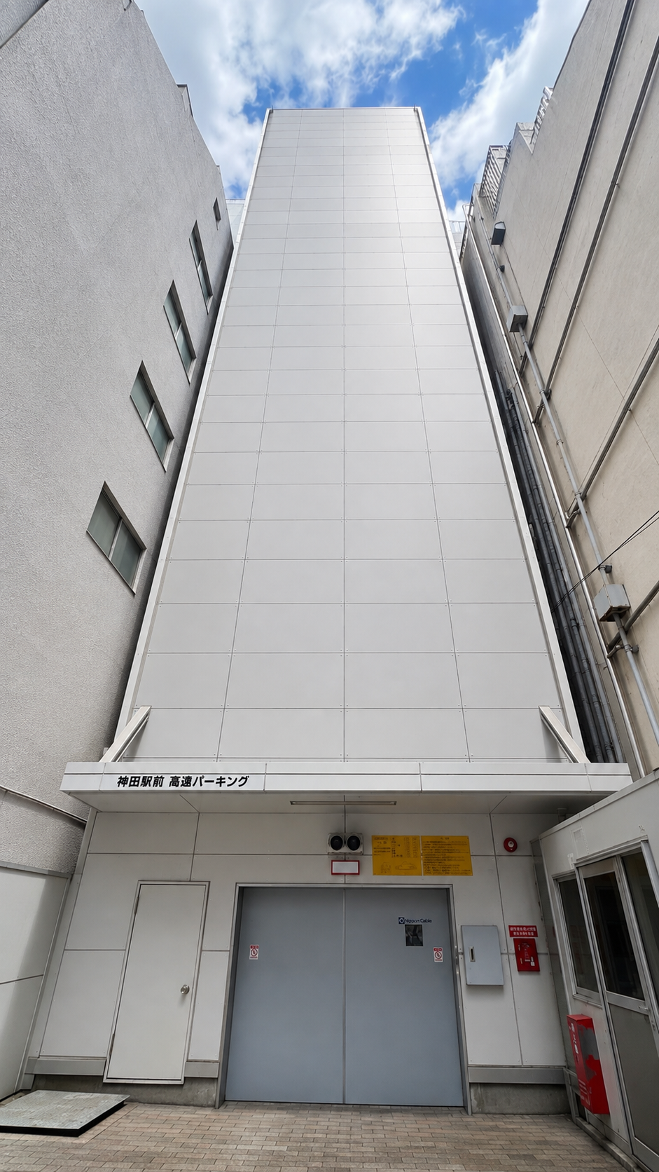 神田駅前高速パーキングの建物の正面の写真。青空と白い雲が見える。