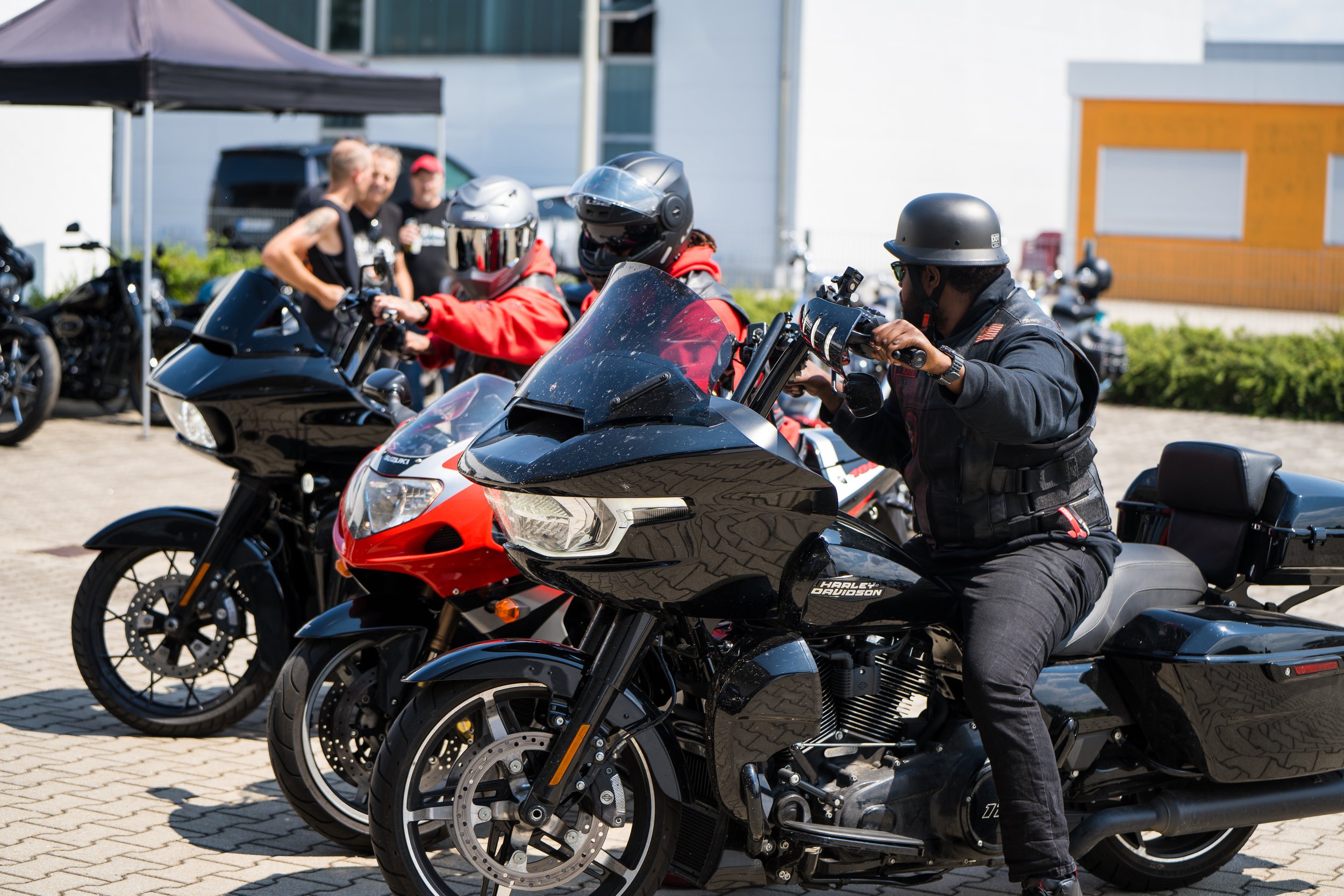 Motorradfahrer vor Motorrädern, im Hintergrund Menschen und Gebäude. Bei der Eröffnungsfeier von Gasolina Custom Motorcycles.
