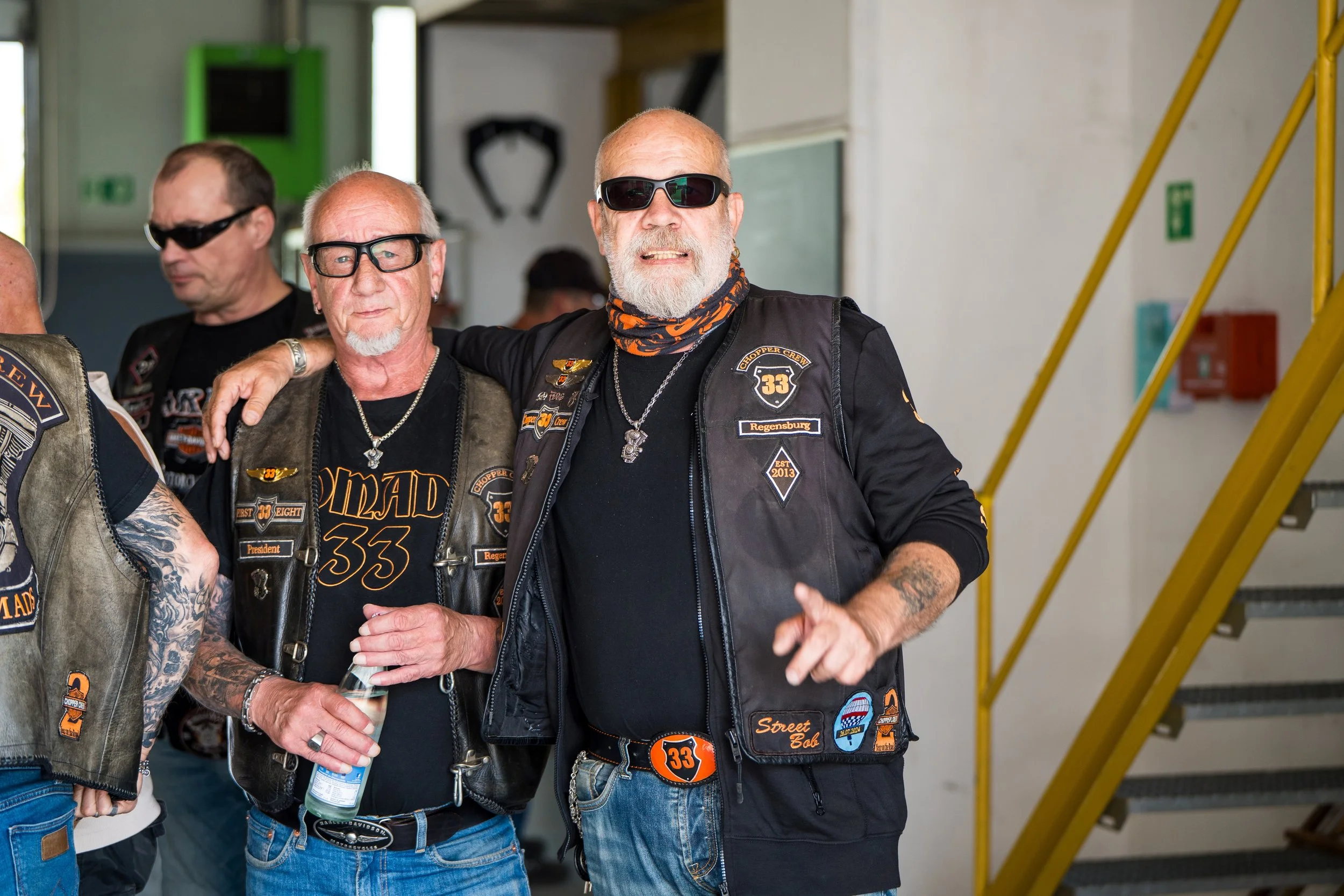Gruppe alter Männer in Biker-Kleidung mit Sonnenbrillen, die lächelnd zusammenstehen.  Bei der Eröffnungsfeier von Gasolina Custom Motorcycles.