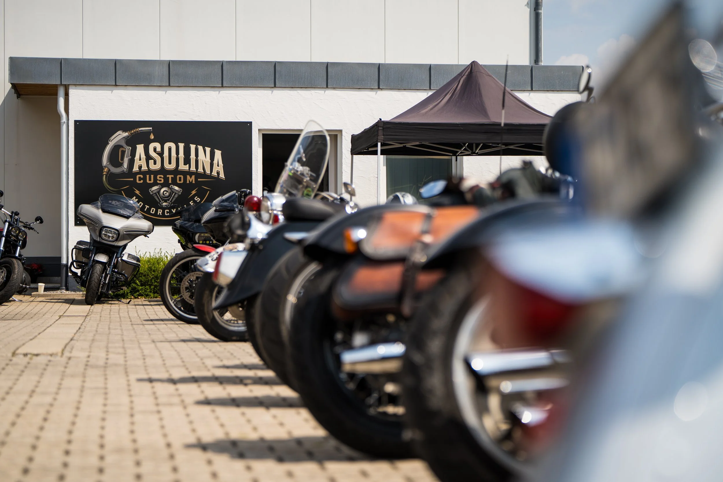 Gasolina Custom Motorcycles Gelände mit geparkten Motorrädern und Gasolina Custom Motorcycles Schild an der Wand