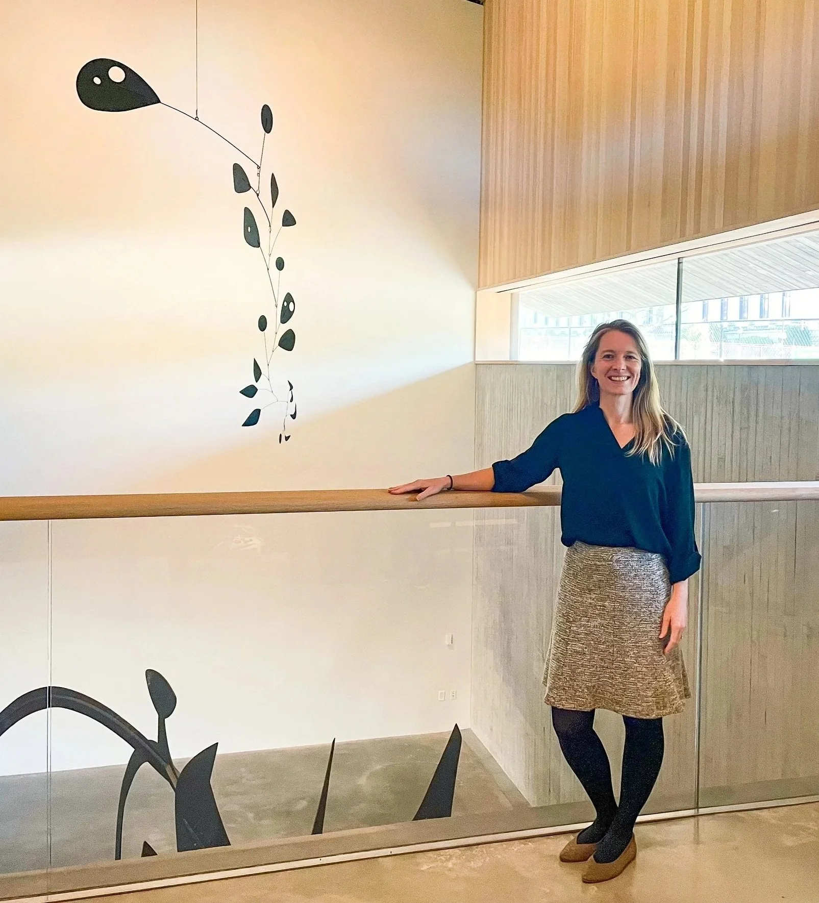 Amy Halliday in a museum setting with some hanging mobile sculpture works by Alexander Calder.