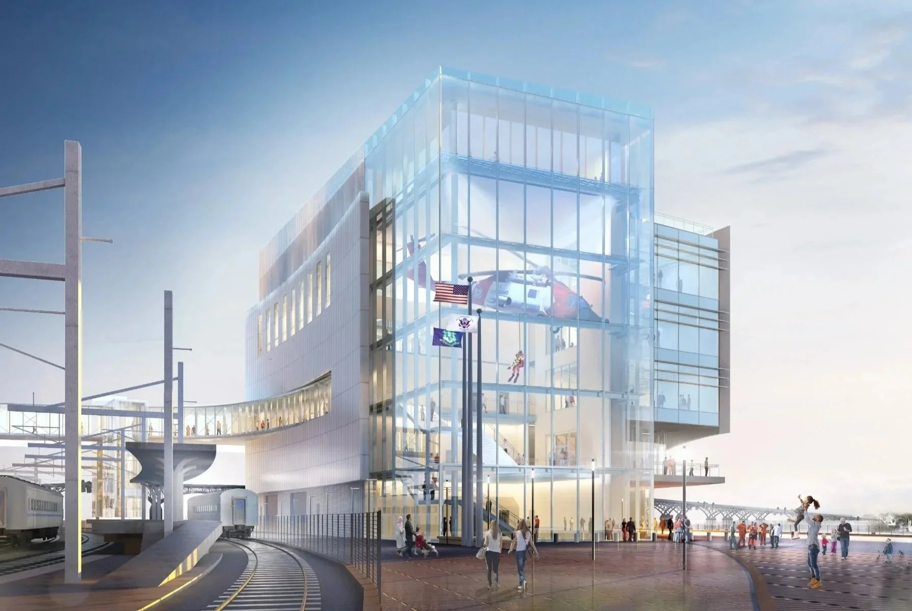 Modern glass building with a helipad, American flags, people walking around, a train, and railway tracks, with a cloudy sky background.