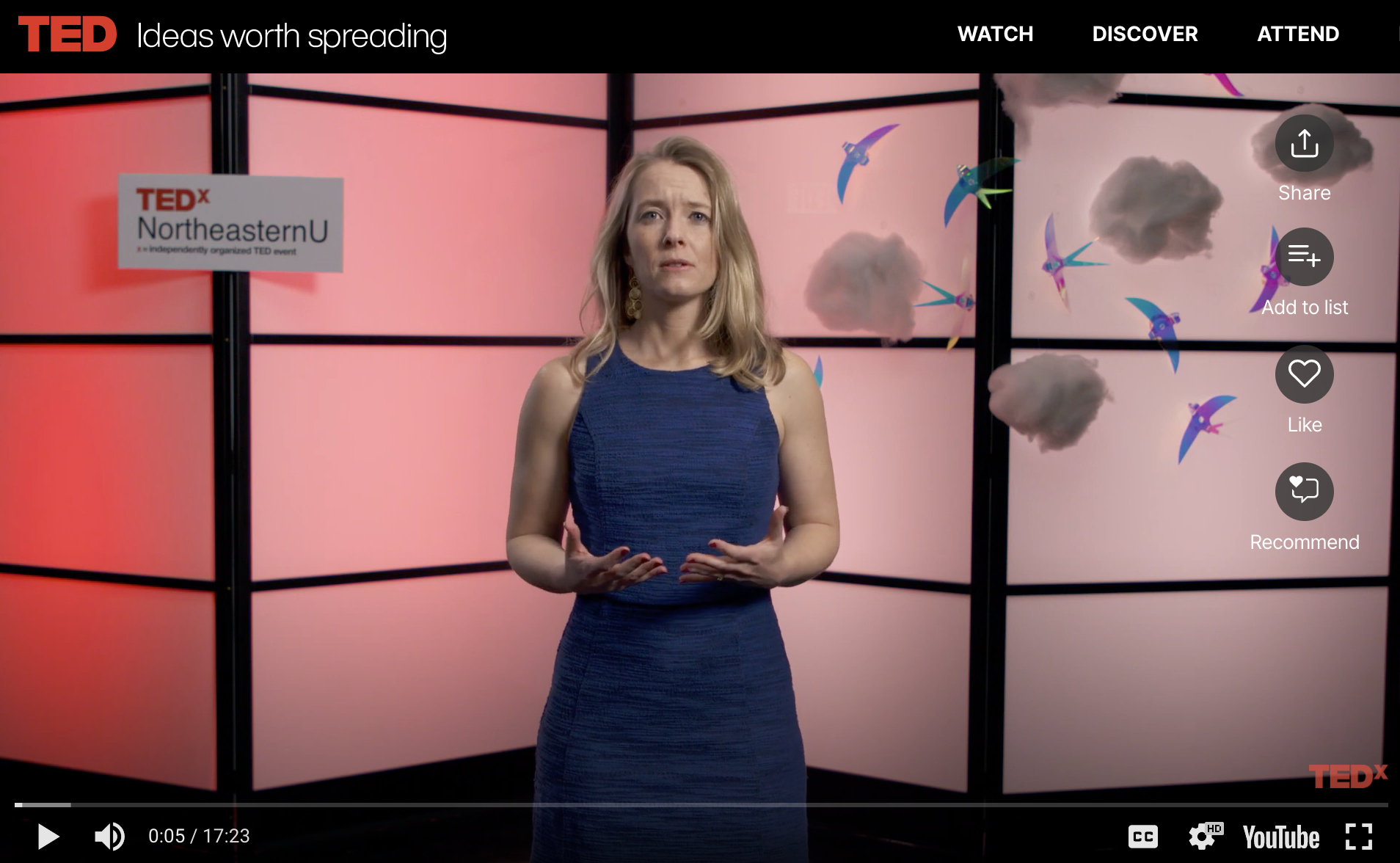 A woman standing in front of a pink background with clouds and colorful birds, with a sign that reads 'TEDx NortheasternU' on her left.