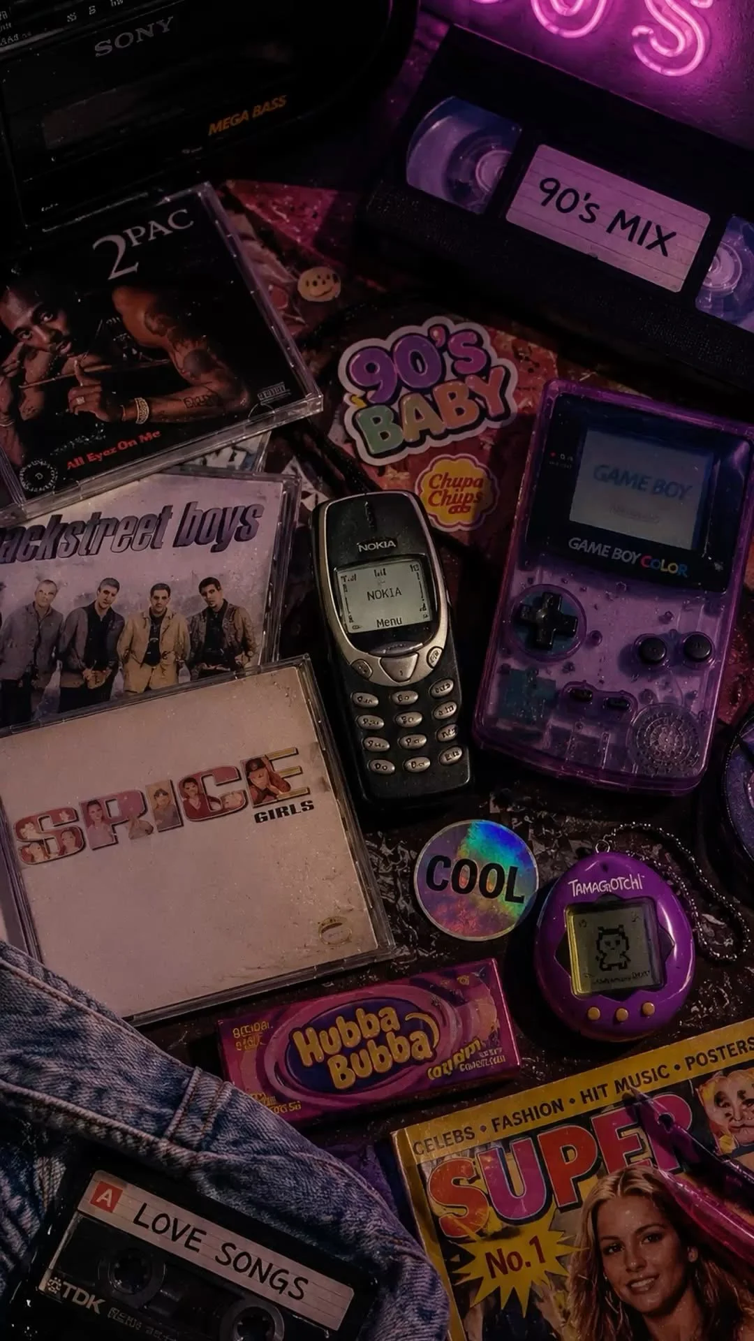 Collection of 90s-themed items including cassette tapes, a pink Game Boy Color, a Nokia phone, a sticker with '90s BABY', a CD case with Backstreet Boys, Spice Girls, 2Pac, and other memorabilia.