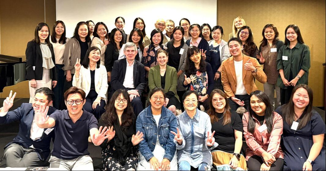 Group photo of diverse adults in a conference room, smiling and making peace signs.