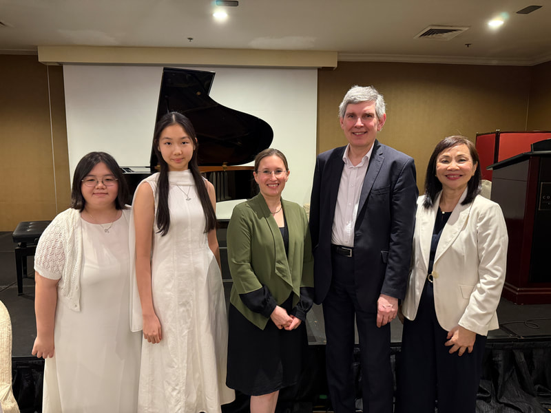 Five people standing on a stage in front of a piano and a speaker, smiling for the camera.