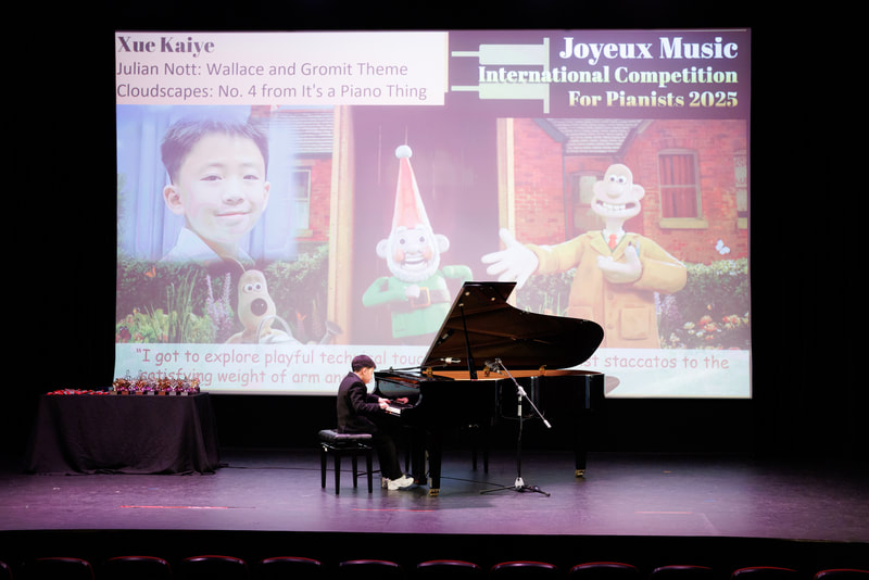 A young boy is playing a grand piano on stage in front of a large colorful screen displaying information about a music competition and animated characters. The screen has text about Xue Kaiye, Julian Nott, and other topics, with cartoon characters and a photo of a boy smiling.