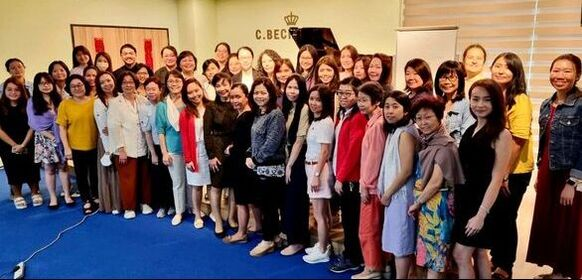 Group photo of women standing in a room with a piano and C.BEC sign, green and yellow walls