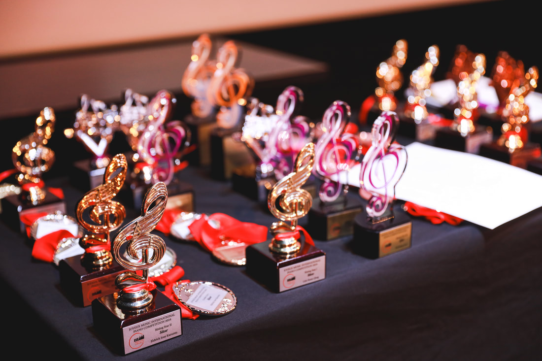 Multiple music trophies, medals, and awards displayed on a black table, likely for a music competition.