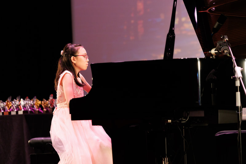 Young girl playing piano on stage at a performance or recital.