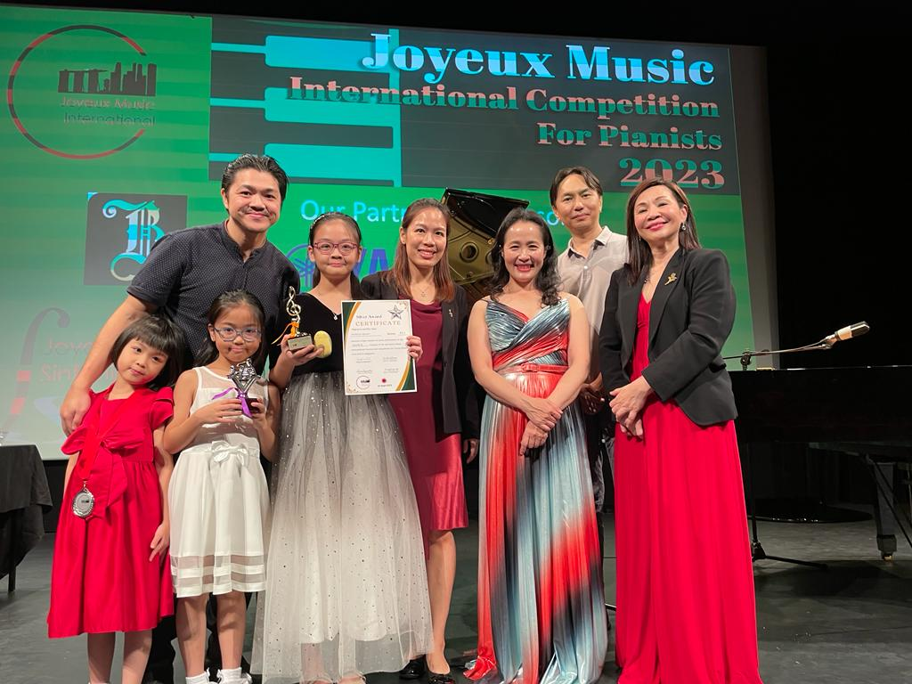 Group of people on stage at the Joyeux Music International Competition for Pianists 2023, with some holding awards and a certificate.