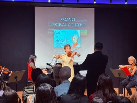 Violinist performing at Mozart Festival Concert with audience and other musicians on stage.