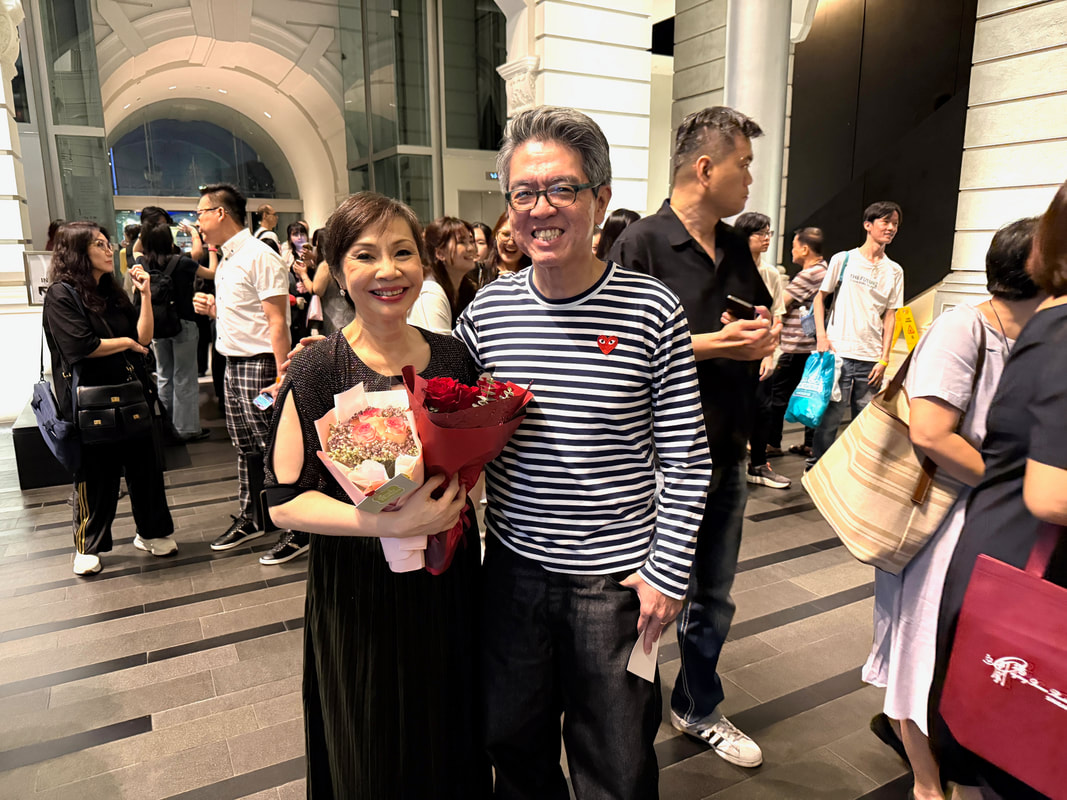 A woman holding a bouquet of flowers standing beside a man at a crowded indoor event.