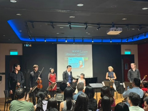Orchestra performing on stage with conductor and audience in front at a concert venue.