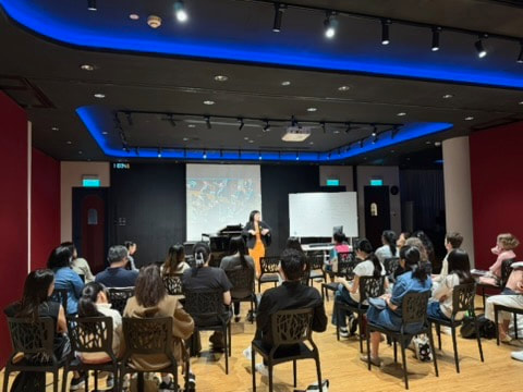 A woman presenting to an audience in a conference room with a projector screen and whiteboard.