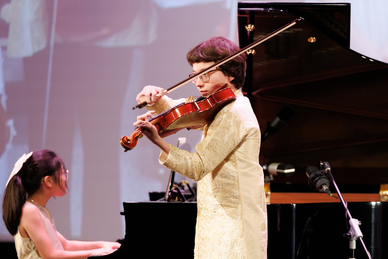 A young girl playing the piano and an older woman playing the violin during a performance on stage.
