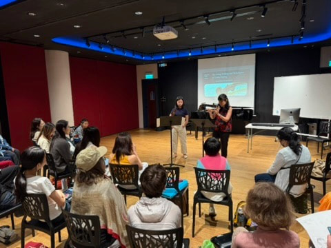 People attending a presentation in a conference room with a large screen and a speaker at a podium.