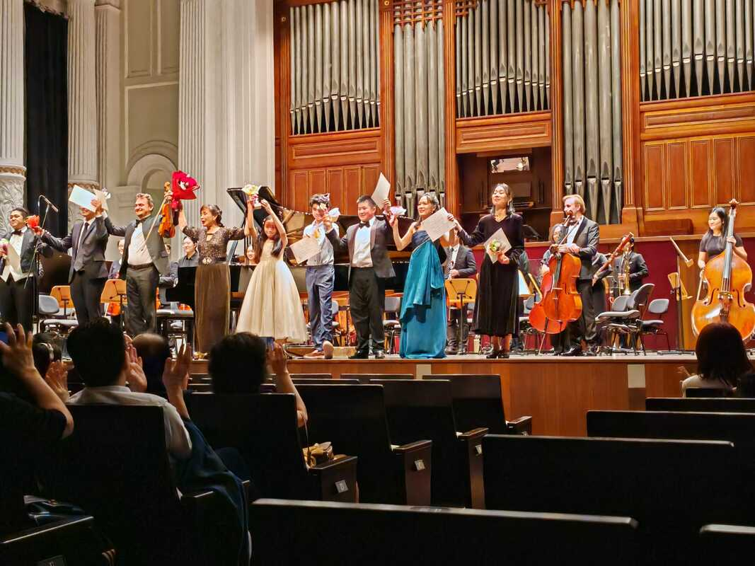 Orchestra performing on stage with musicians and audience clapping.