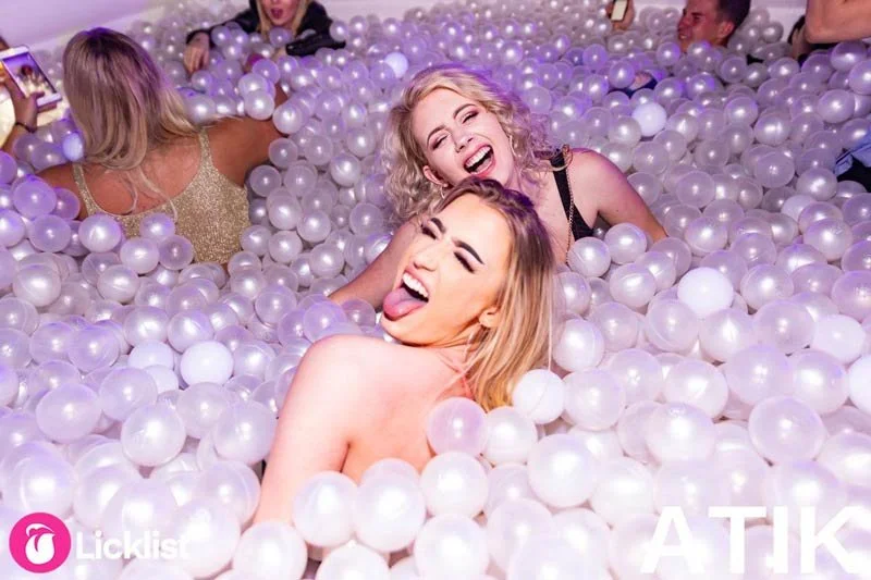 Three friends lying together in a white and pearl ball pit at a nightclub