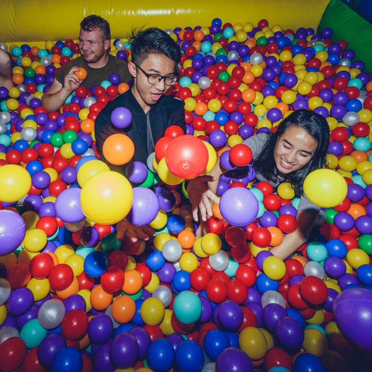 Four friends throwing brightly coloured ball pit balls into the air