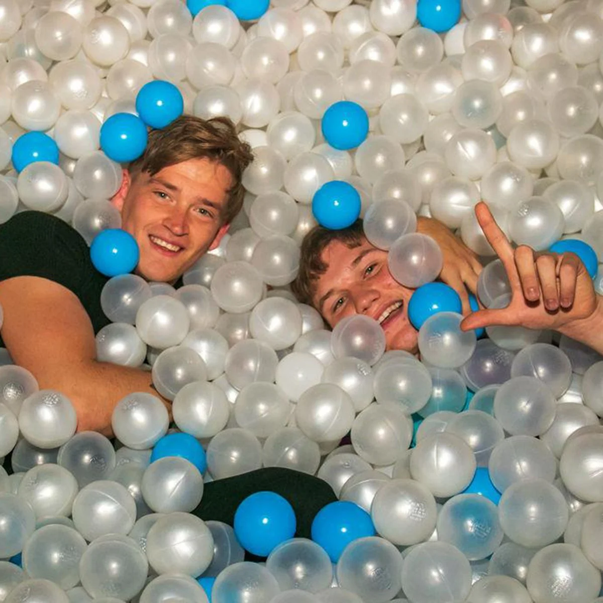 Two men lying back in a pearl and blue ball pit at a party
