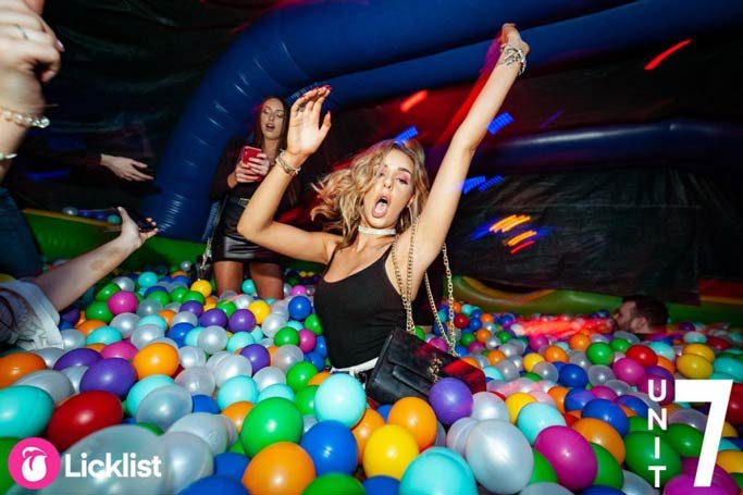 Woman celebrating with her arms in the air in an inflatable ball pit on a nightclub dancefloor