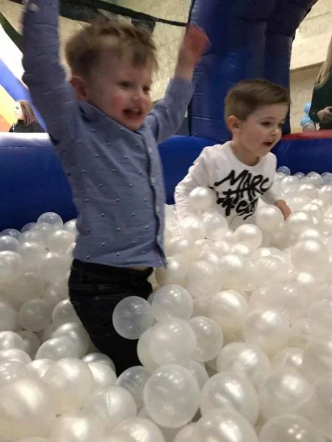 Two young boys playing in a white pearl ball pit at a family event