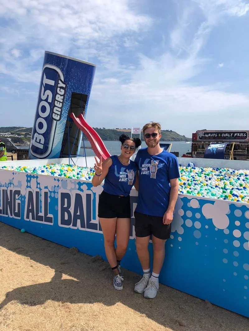 Event staff beside a branded blue and white ball pit at a seaside Boost Energy activation
