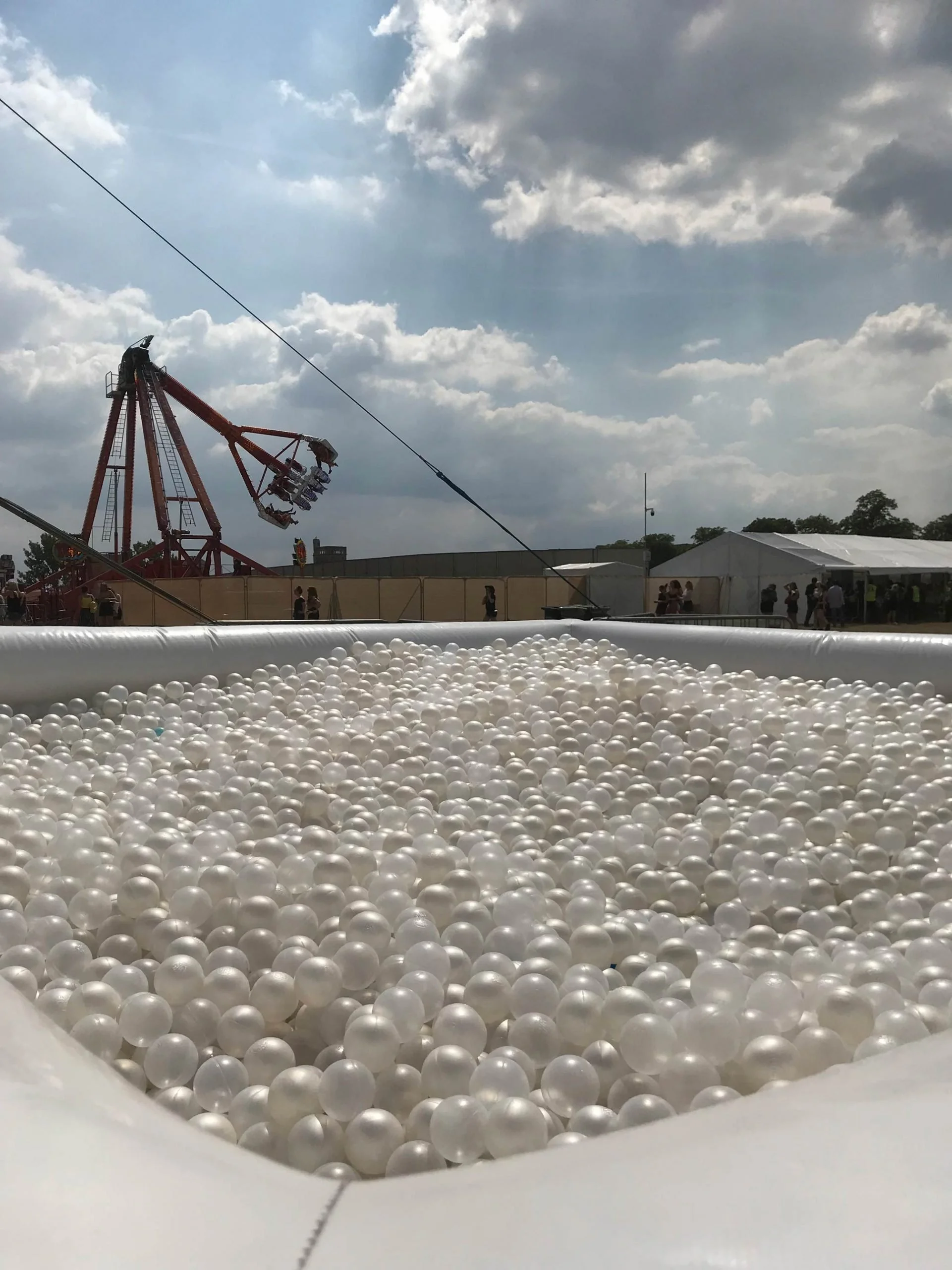 Large outdoor ball pit filled with white pearl balls at a funfair
