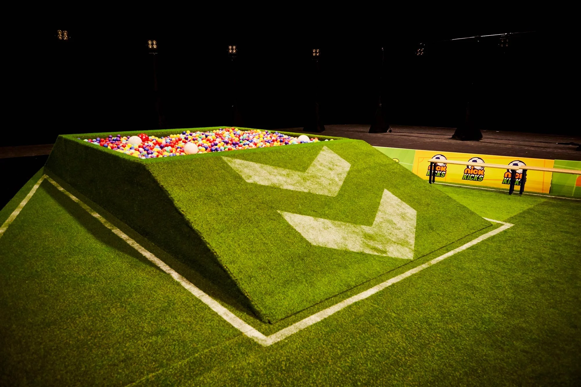 Ball pit built into a raised grass stage set, lit at night for a brand event