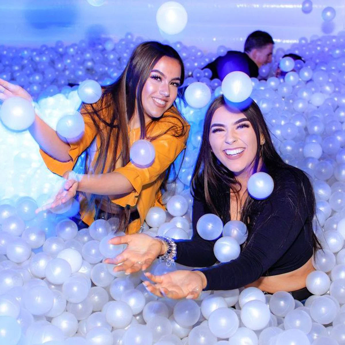 Two women throwing pearl ball pit balls into the air at an event
