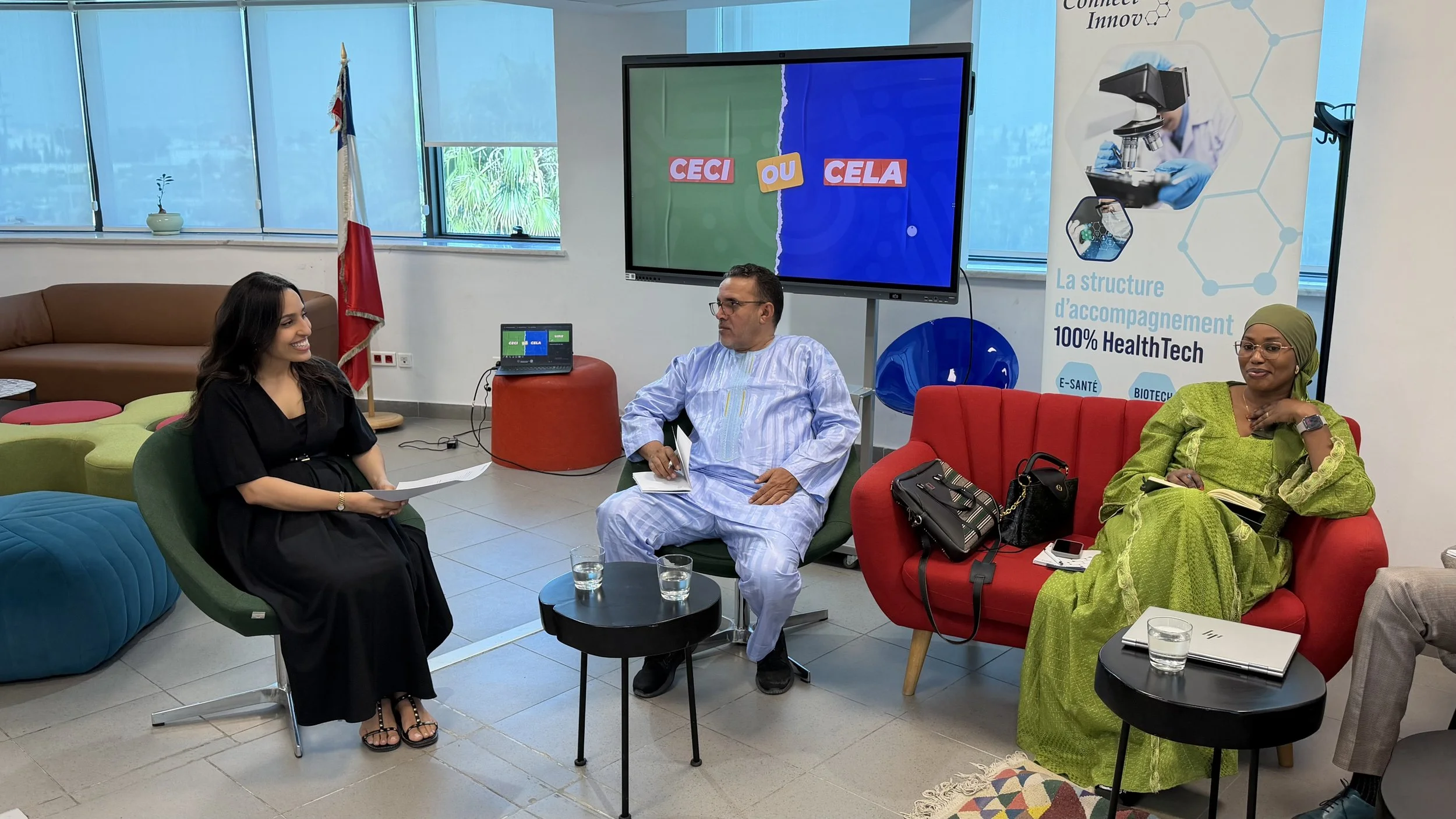 Une réunion avec trois personnes dans une salle moderne, deux femmes et un homme, discutant. Un grand écran affiche 'Ceci ou Cela'. Un panneau indique 'Connect Innov' et des thèmes liés à la technologie de la santé.