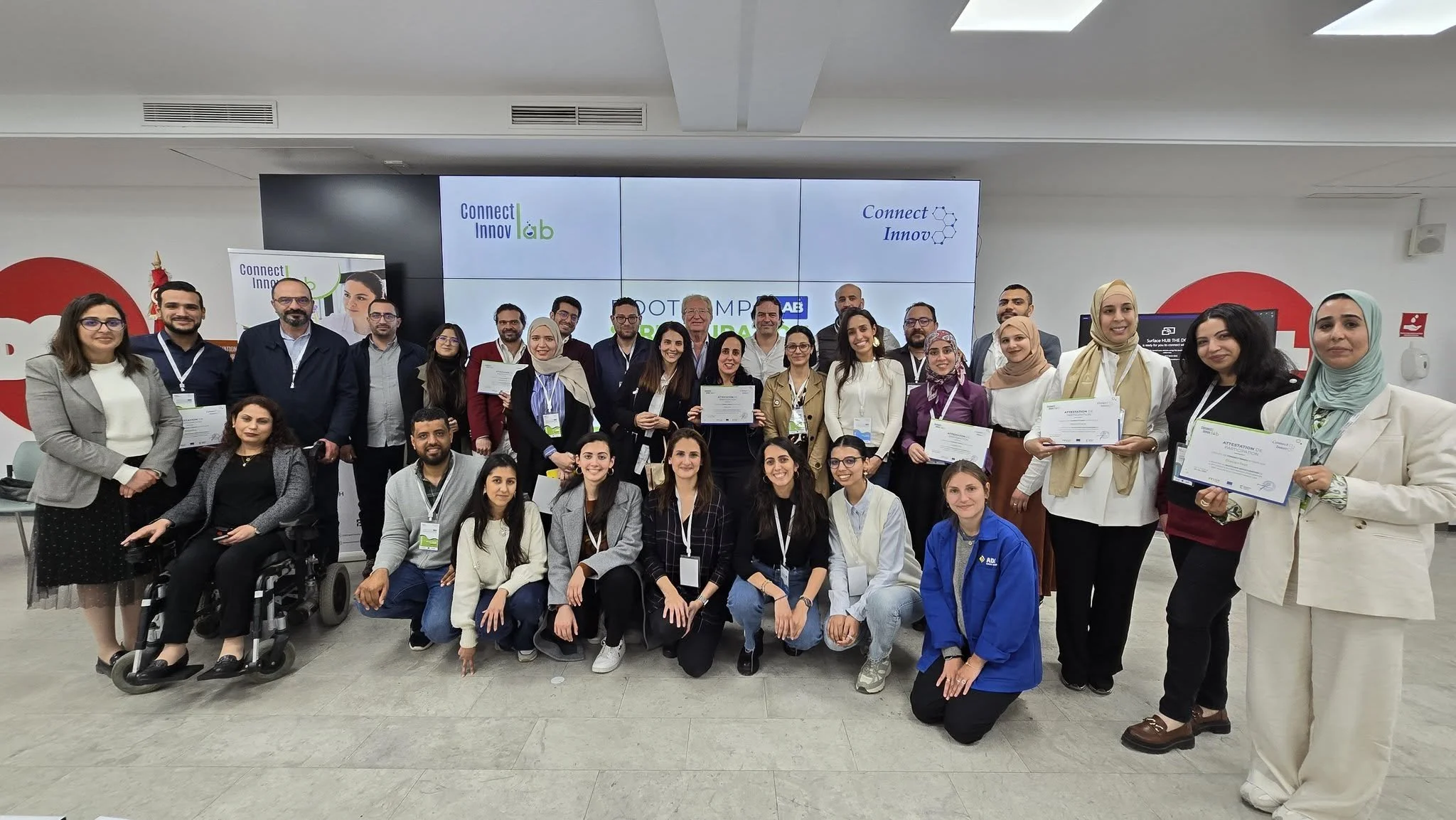 Groupe de personnes posant pour une photo lors d'une cérémonie de remise de diplômes ou d'une formation, certains tenant des certificats, dans une salle avec un grand écran en arrière-plan portant le logo "Connect Innov lab".