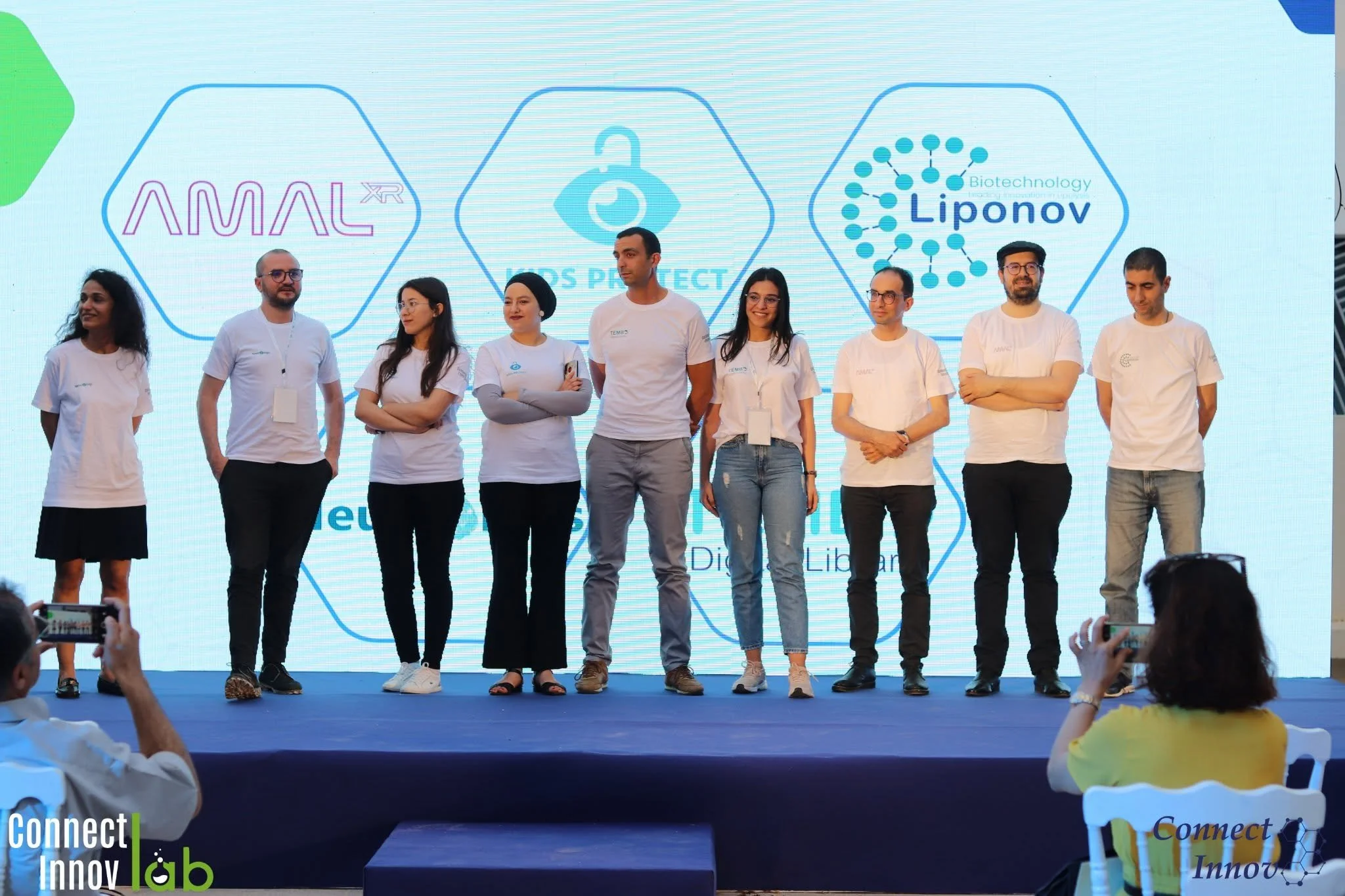 Groupe de huit personnes debout sur scène lors d'une présentation ou d'une conférence, avec un grand écran en arrière-plan affichant des logos liés à la biotechnologie et à l'innovation