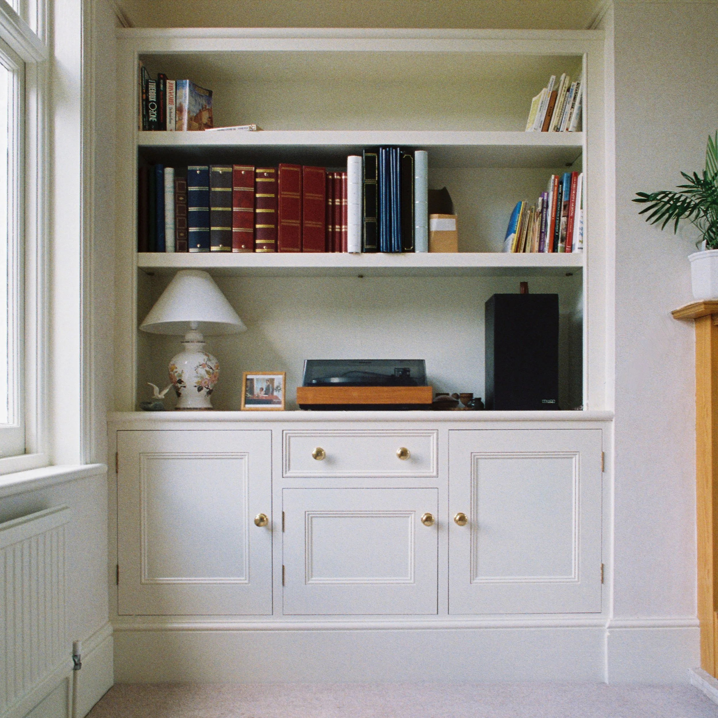 White painted built-in cupboard and bookshelf with adjustable shelves, solid wood framed doors and drawer.